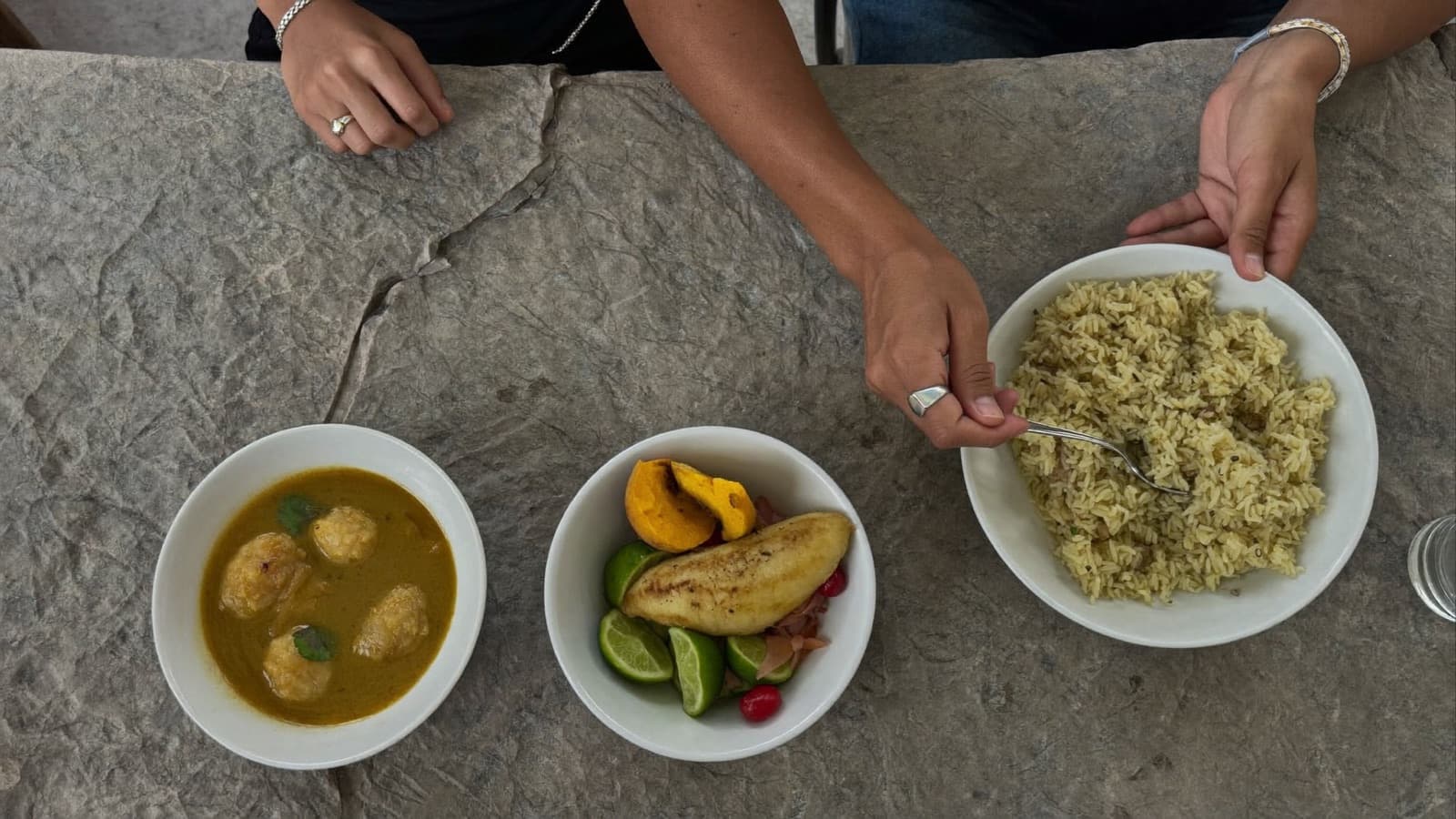 Foto de cima de uma mesa de família com dal, arroz jollof e ceviche