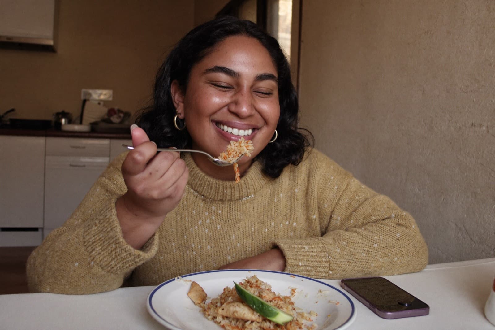 Mulher comendo à mesa da cozinha com o celular ao lado do prato