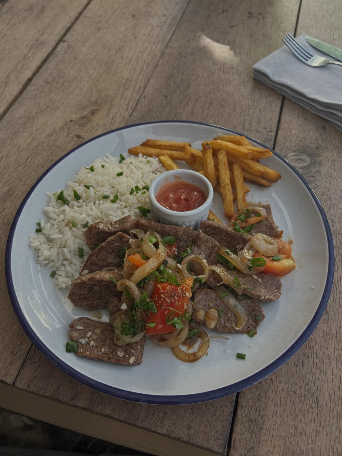 Prato de lomo saltado peruano com arroz e batatas fritas em mesa de madeira